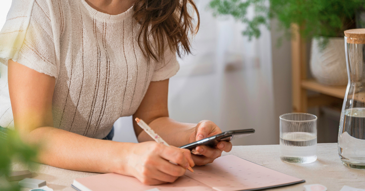 Woman writing while looking at her phone