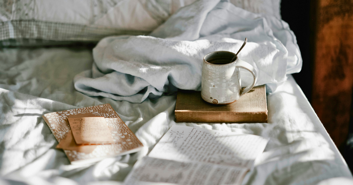 Books, papers and a coffee mug spread across a bed